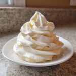 A beautiful, tall swirl of creamy white vanilla buttercream frosting piped onto a small white dish.