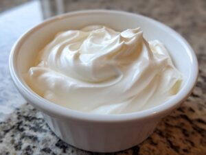 Close-up of thick, glossy white royal icing in a small white bowl, ready for the cookie icing recipe.