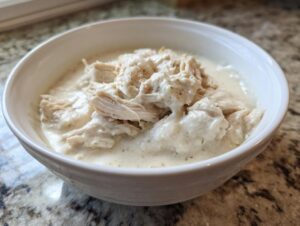 Close-up of a white bowl filled with rich, creamy homemade cream of chicken soup topped with generous shreds of white meat chicken.
