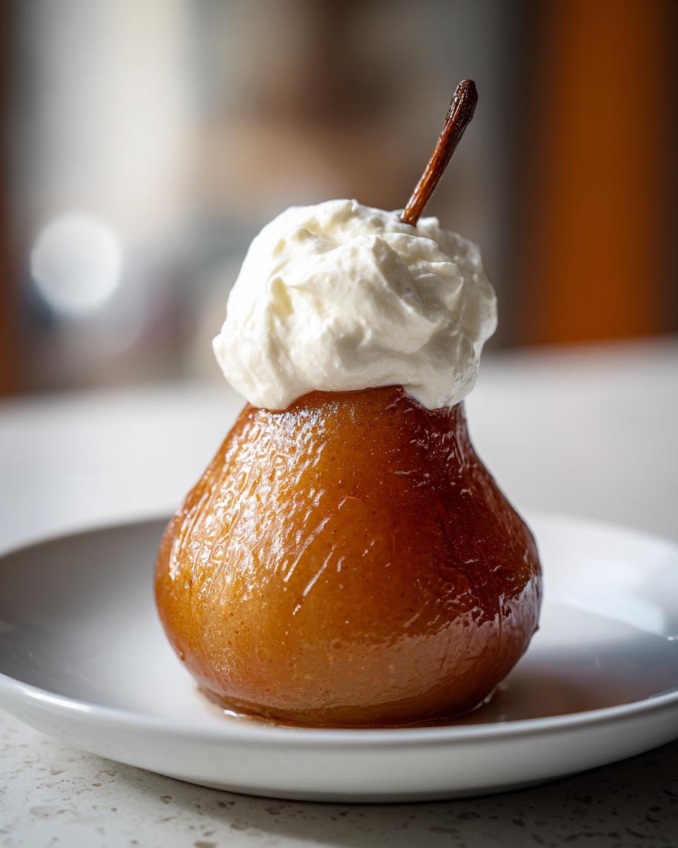 A single, beautifully caramelized poached pear topped with a dollop of fresh whipped cream, served on a white plate.