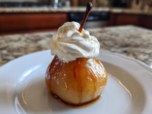 A single, glistening poached pear topped with a dollop of whipped cream, served on a white plate.