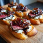 Close-up of a delicious steak crostini bite topped with rare steak, goat cheese, and balsamic caramelized onions.