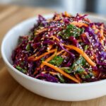 Close-up of a vibrant Asian cabbage salad featuring shredded purple cabbage, carrots, and sesame seeds.