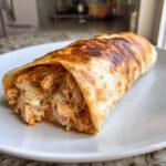 Close-up of a golden-brown Baked Chicken Chimichangas, showing shredded chicken and melted cheese spilling out.
