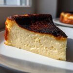 A close-up slice of creamy Basque cheesecake showing its signature dark, caramelized top.