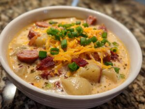 Close-up of a creamy bowl of Cajun potato soup topped with sausage, shredded cheese, and green onions.
