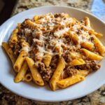 A close-up of a hearty serving of cheesy beef pasta made with penne, rich meat sauce, and melted mozzarella.