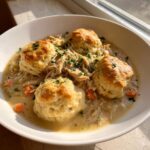 A close-up bowl of creamy chicken and dumplings with biscuits, topped with fresh parsley.