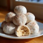 A stack of delicious cinnamon sugar snowball cookies coated in powdered sugar, with one cookie broken in half showing the soft interior.