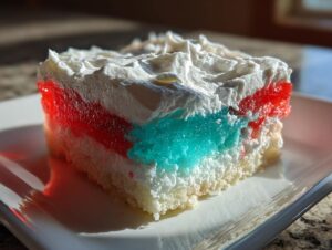 A close-up slice of a colorful jello poke cake featuring red and blue gelatin layers over white cake, topped with whipped cream.