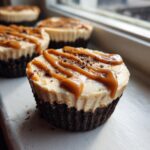 A close-up of a single cookie butter cheesecake cup topped with caramel drizzle and cookie crumbs.