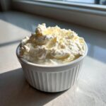 A close-up of fluffy, white creamy horseradish sauce mounded high in a small, white, ribbed ramekin.