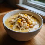 A close-up of a bowl of creamy white chicken chili topped with shredded chicken, white beans, and corn.
