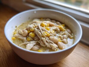 Close-up of a white bowl filled with creamy white chicken chili, featuring shredded chicken, white beans, and corn kernels.