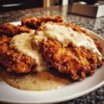 Close-up of golden, crispy chicken fried steak smothered in creamy black pepper gravy on a white plate.