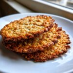 A stack of three golden brown, crispy oatmeal lace cookies resting on a white plate.