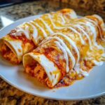 Two rolled easy chicken enchiladas covered in red sauce, melted cheese, and drizzled with sour cream.