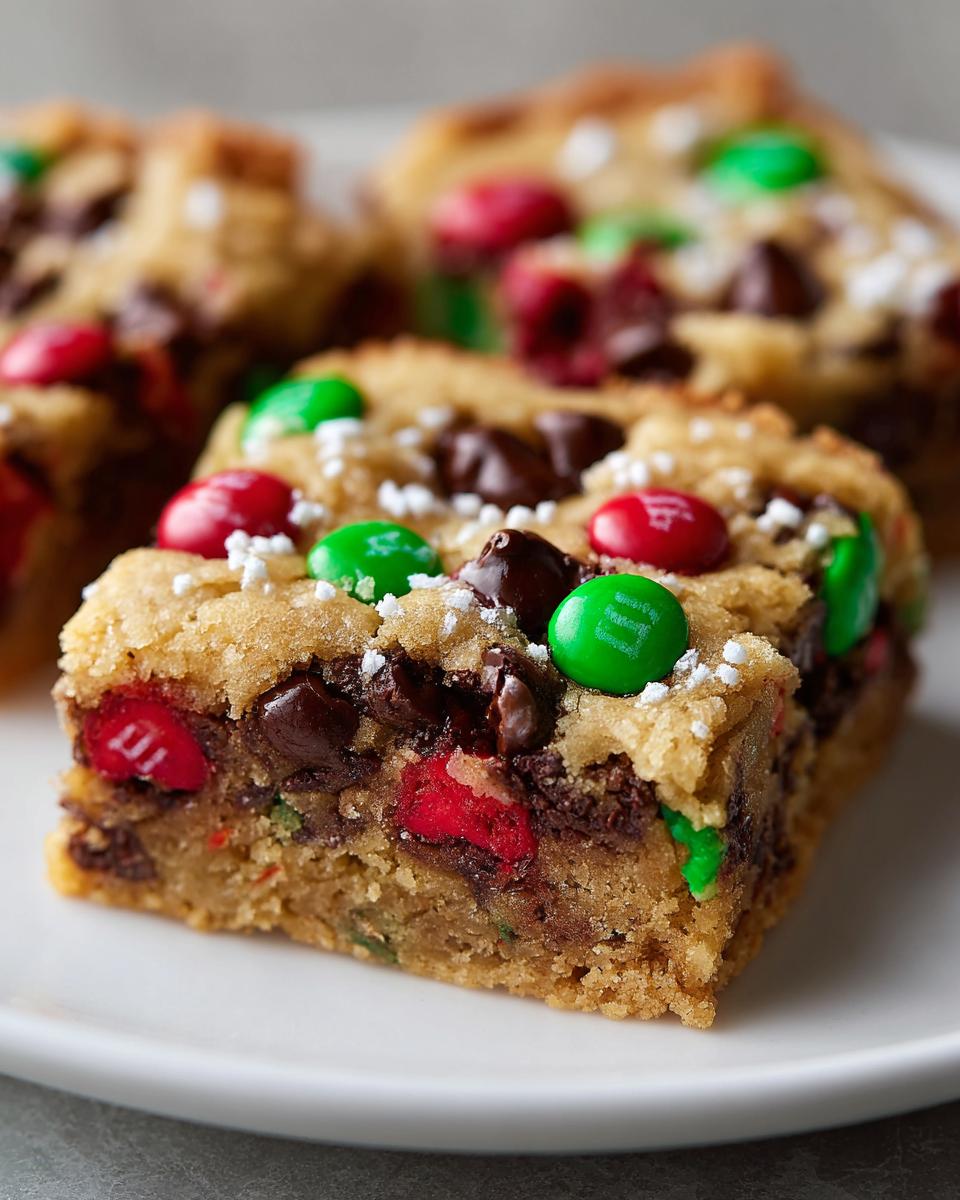 A close-up of a thick, chewy slice of christmas cookie bars studded with red and green M&Ms and chocolate chips.