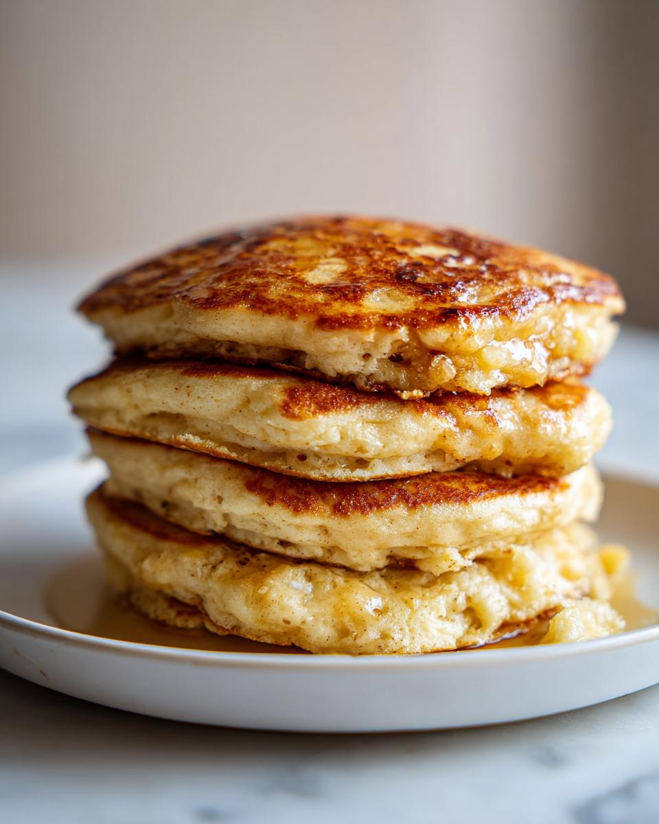 Close-up of a tall stack of four fluffy banana pancakes drizzled with syrup.