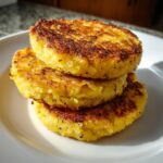 A stack of three golden, pan-fried cornbread rounds with crispy, browned edges on a white plate.