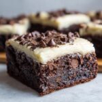 A close-up shot of a fudgy banana bread brownies square topped with thick white frosting and chocolate chips.