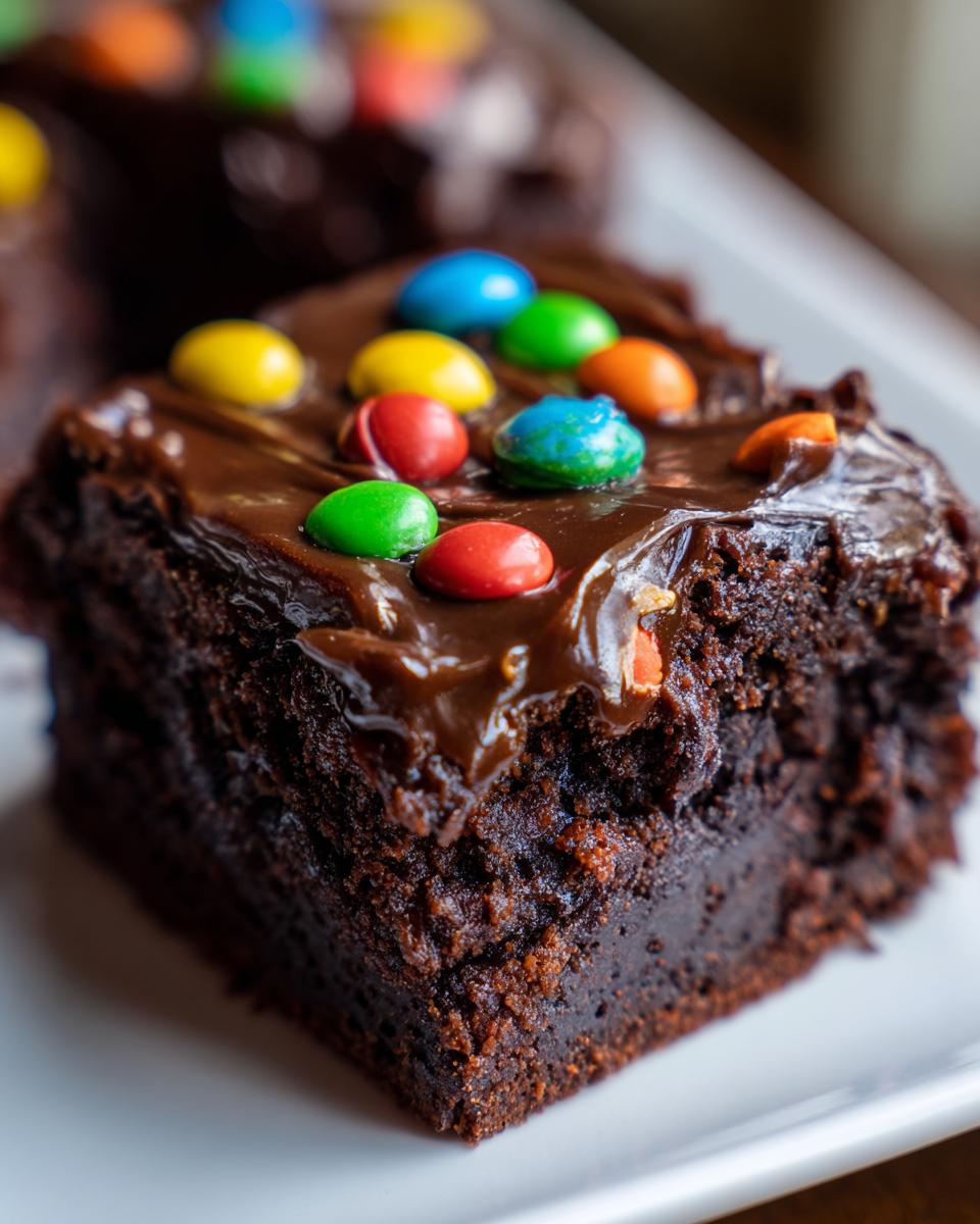 A close-up of a rich, fudgy square of cosmic brownies topped with glossy chocolate frosting and colorful candy pieces.