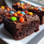 A moist, dark chocolate slice of cosmic brownies topped with fudge frosting and colorful candy pieces.