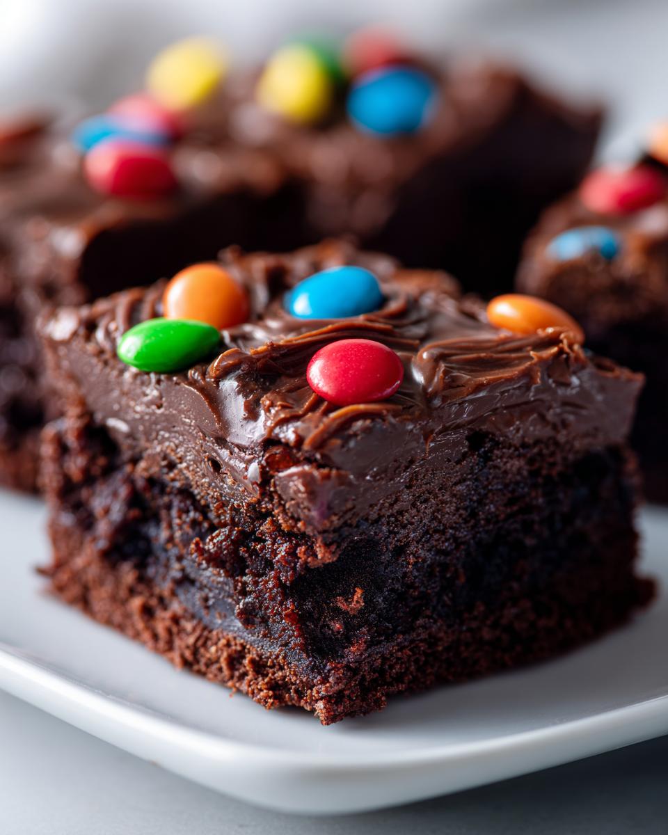 Close-up of a fudgy square of cosmic brownies topped with rich chocolate frosting and colorful candy-coated chocolates.