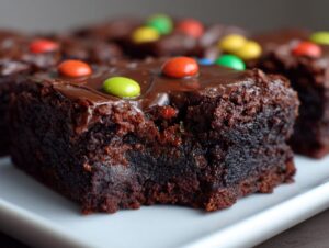 A close-up of a rich, fudgy square of cosmic brownies topped with chocolate glaze and colorful candy pieces.