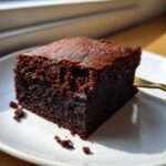 A close-up, fudgy square of dark chocolate gingerbread brownies resting on a white plate.