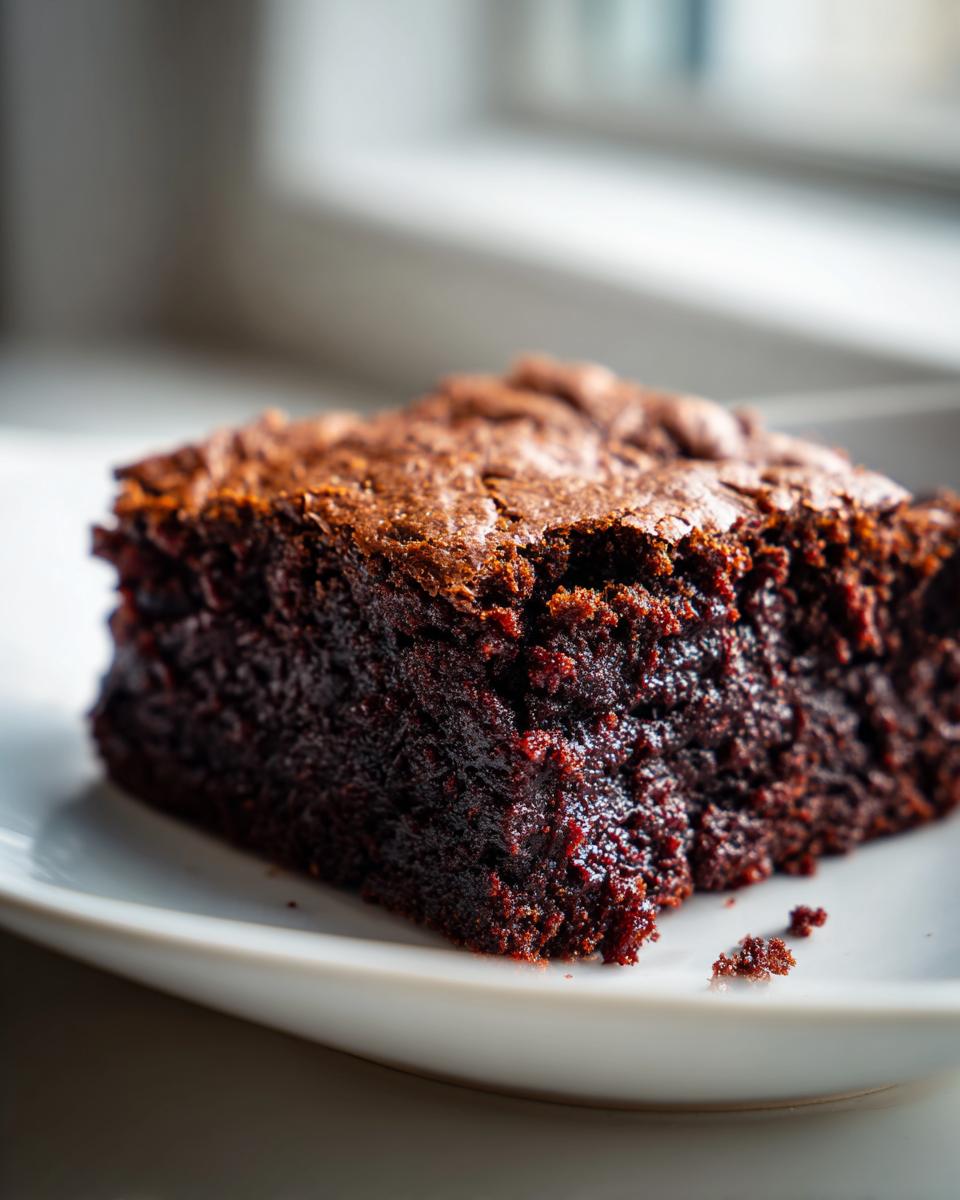 Close-up of a rich, dark, fudgy slice of gingerbread brownies on a white plate.