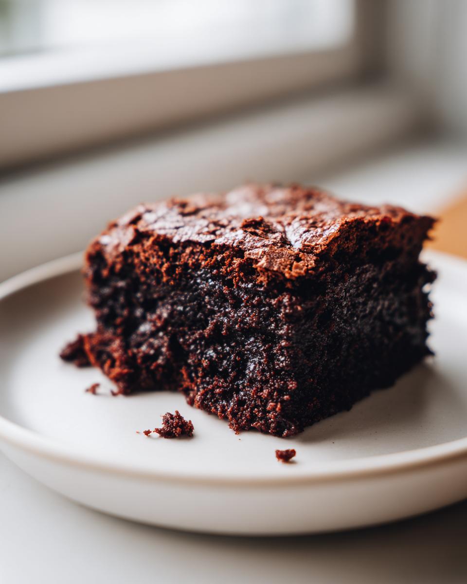 A close-up of a dark, fudgy slice of gingerbread brownies sitting on a light-colored plate.