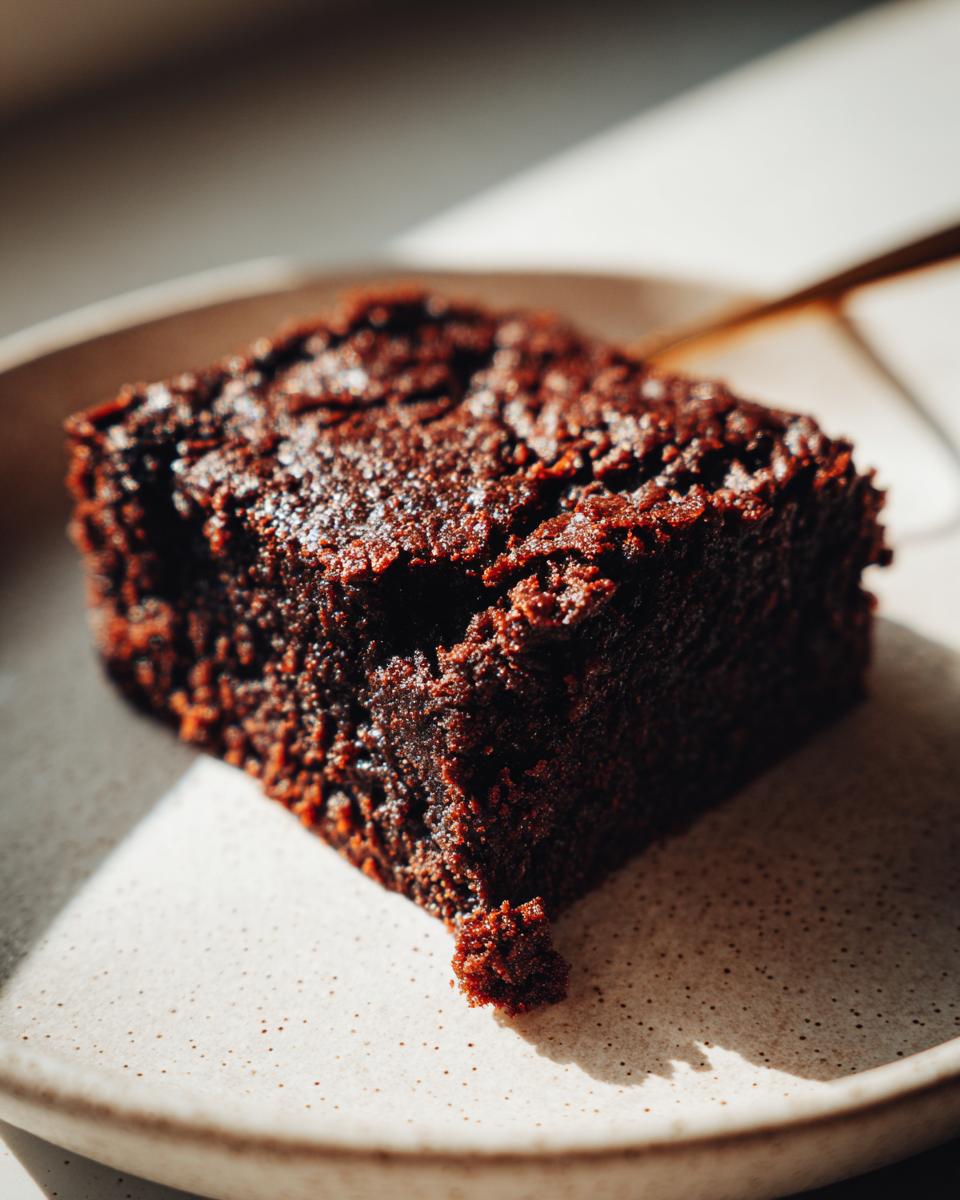 Close-up of a rich, dark, fudgy gingerbread brownies square sitting on a speckled ceramic plate.