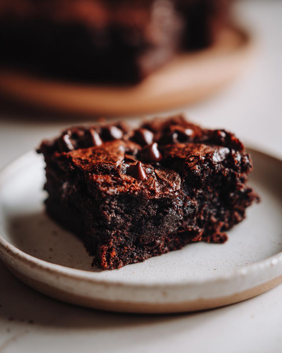 Close-up of a rich, fudgy slice of sweet potato brownies topped with melted chocolate chips on a light ceramic plate.