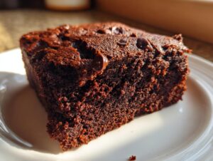 Close-up of a rich, fudgy slice of sweet potato brownies topped with melted chocolate chips on a white plate.