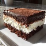 A rich slice of Italian love cake showing three distinct layers: chocolate cake, white cream filling, and a chocolate ganache topping dusted with cocoa.