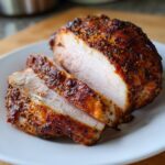 Close-up of juicy baked chicken breast, sliced to show the seasoned crust and tender white interior.