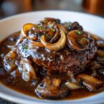 A close-up of a juicy Salisbury steak smothered in rich brown gravy, topped with sautéed mushrooms and onions.