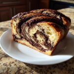 A close-up of a thick slice of moist chocolate babka showing beautiful dark chocolate swirls in the golden bread.