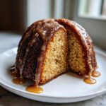 A slice of moist rum cake recipe, drizzled heavily with a thick, glistening caramel sauce, served on a white plate.