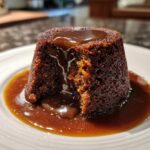 Close-up of a moist sticky toffee pudding recipe portion, cut open to show the rich texture, covered in thick toffee sauce.