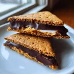 Two halves of a no bake buckeye graham crackers sandwich stacked on a white plate, showing chocolate and peanut butter filling.