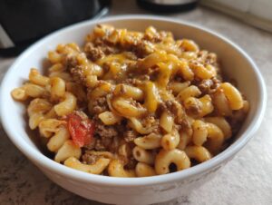 Close-up of a hearty bowl of cheesy taco pasta mixed with ground beef and tomatoes.