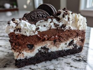 A close-up slice of a multi-layered ice cream cake featuring chocolate mousse, vanilla, and an Oreo crust, topped with whipped cream.