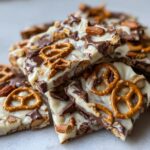 Close-up of stacked pieces of peanut butter pretzel bark topped with white chocolate, milk chocolate chunks, and mini pretzels.