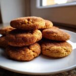 A stack of soft, freshly baked pumpkin snickerdoodle cookies coated in cinnamon sugar on a white plate.