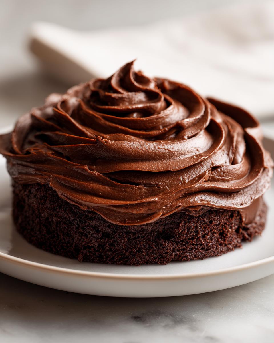 A small, dark chocolate cake generously topped with swirls of rich chocolate frosting.