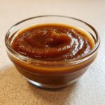 Close-up of rich, dark brown pear butter swirled beautifully in a small, clear glass bowl.