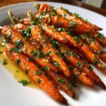 Close-up of glossy, glazed roasted baby carrots topped with fresh parsley and garlic sauce.