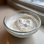 A clear glass bowl filled with thick, glossy white royal icing recipe mixture, ready for decorating.